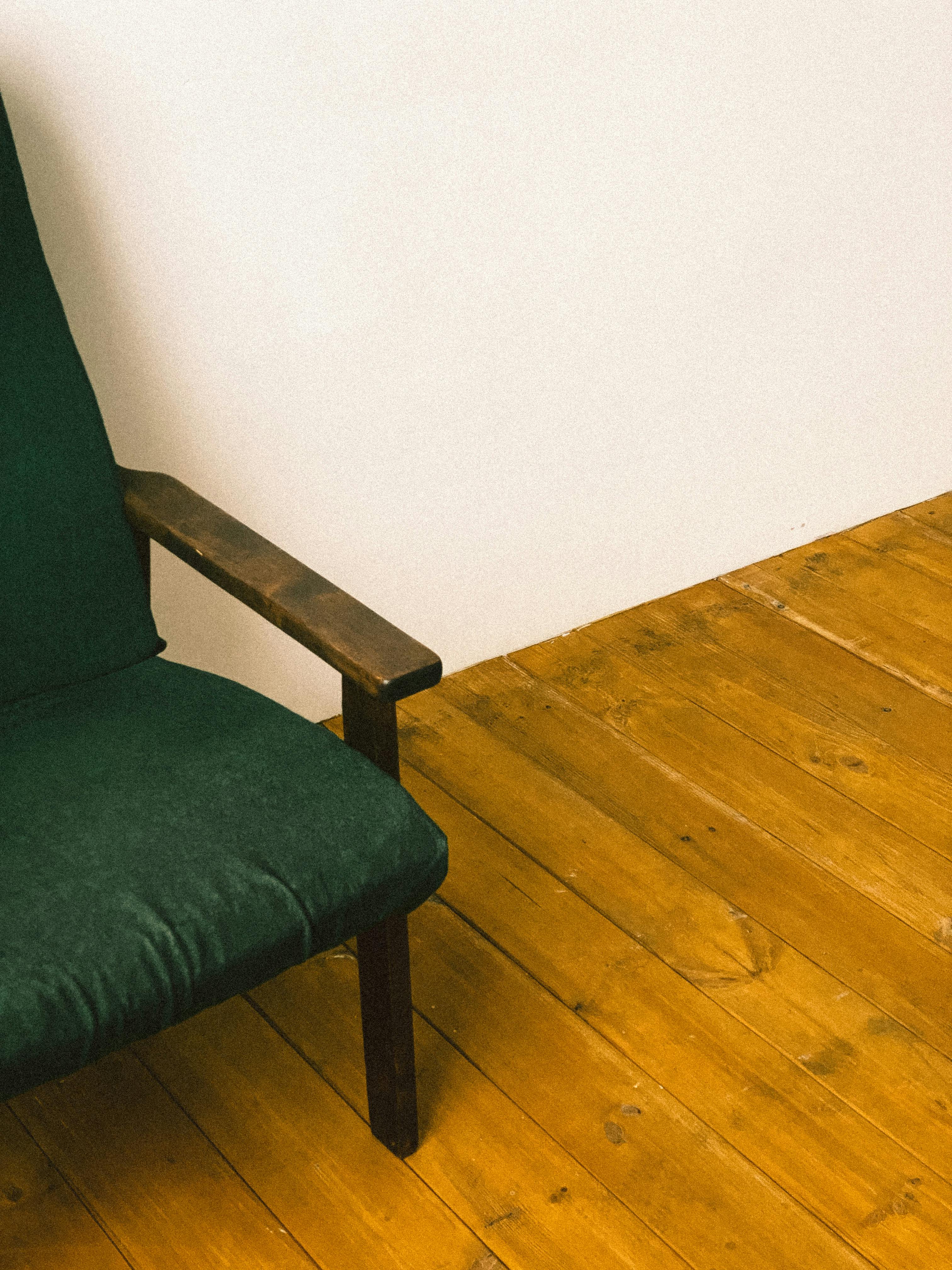 Free A green armchair beside a white wall on a wooden floor, offering a warm, rustic feel. Stock Photo