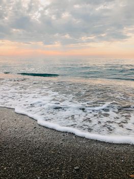 Peaceful ocean waves on a pebble beach at sunset in Sochi, Russia.
