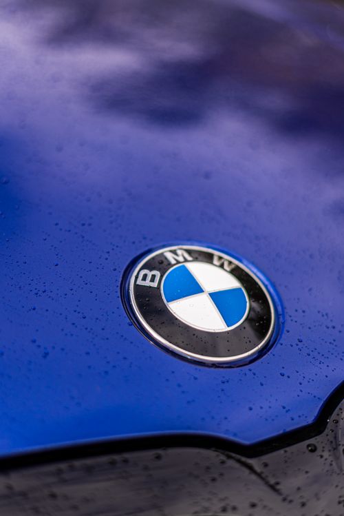 Free A detailed shot of the BMW emblem on a wet blue car, highlighting luxury and elegance. Stock Photo