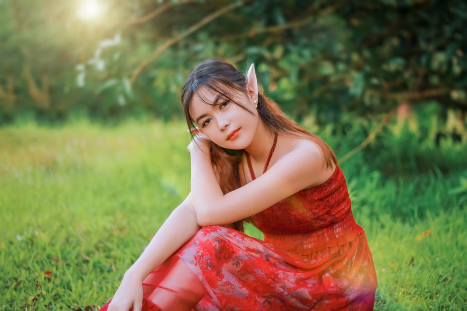 A young woman in elf cosplay sits gracefully in a vibrant summer field.