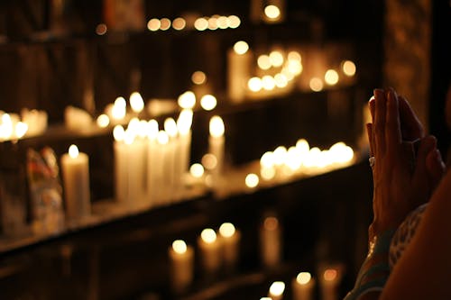 Крупным планом фотография человека, молящегося перед выстроенными свечами