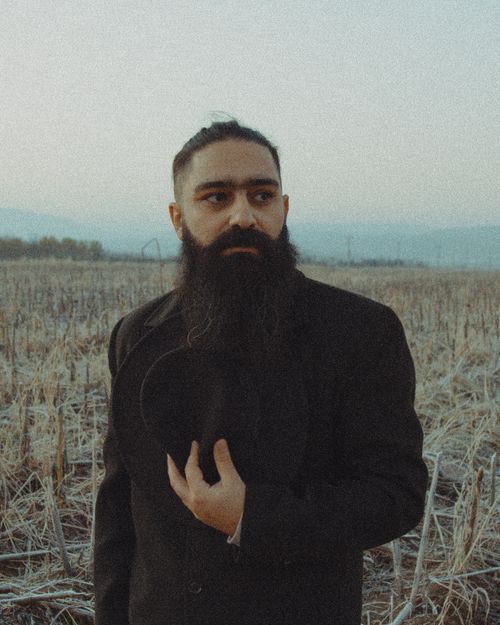 Free Portrait of a bearded man in a frosty field, holding a hat, with a distant horizon. Stock Photo