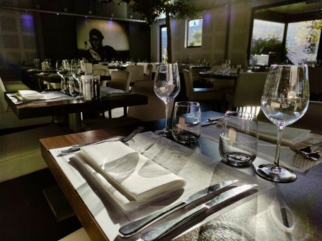 Sunlit restaurant table setting with wineglasses and cutlery, creating a warm dining atmosphere.