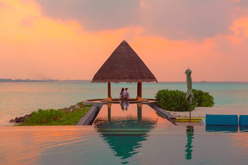Free Couple Under Hut Beside Sea and Infinity Pool Stock Photo