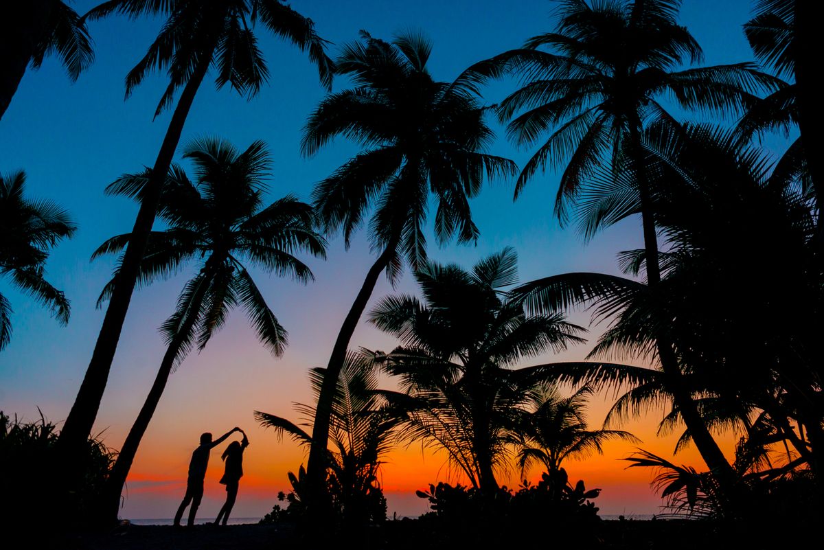 Siluetas de dos personas junto a palmeras durante un atardecer en la playa
