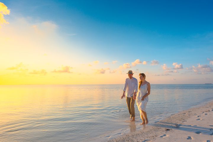 Casal de mãos dadas caminhando na praia ao pôr do sol