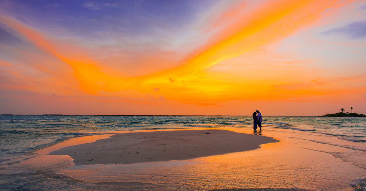 Photo by Asad Photo Maldives Couple shares a romantic moment on a serene tropical beach at sunset, surrounded by vibrant colors.