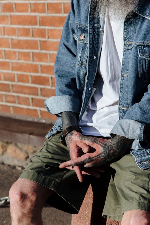 Free Close-up of a tattooed man sitting against a brick wall outdoors. Stock Photo