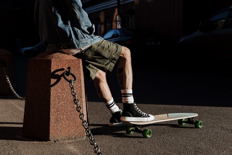 Legs Of Sitting Man In Shorts And Converse Stepping On Skateboard