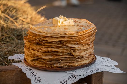 A large stack of crepes topped with butter, set against a rustic outdoor backdrop, perfect for food photography.