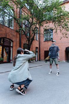 A woman photographer captures a male skateboarder during an outdoor photoshoot in a brick building setting.