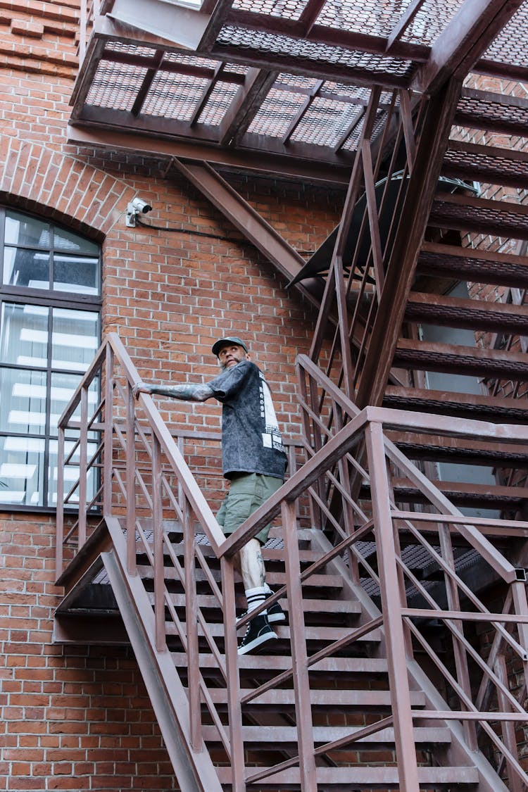 Tattooed Man In T-shirt And Shorts Going Upstairs On Outdoor Staircase