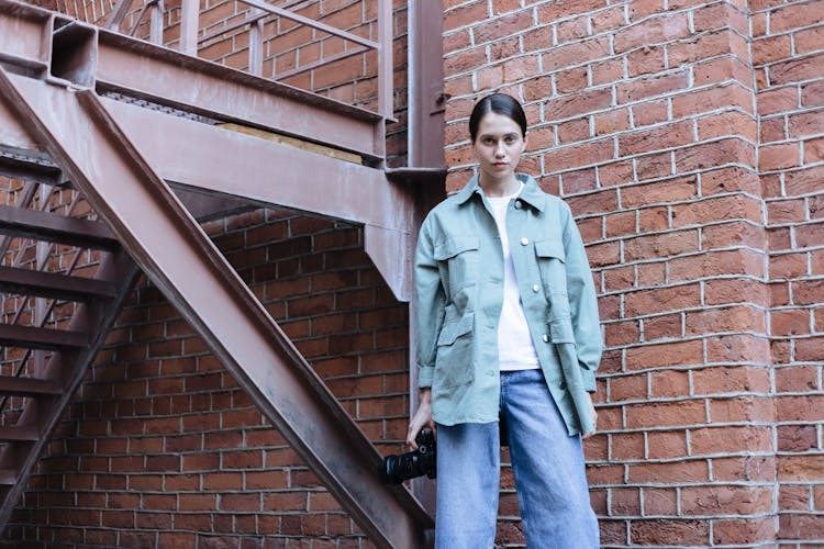 Female Photographer Holding Camera In Hand And Standing At Emergency Stairs