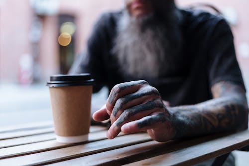 Tattooed Hand of Unrecognizable Man Sitting at Table of Outdoor Cafe