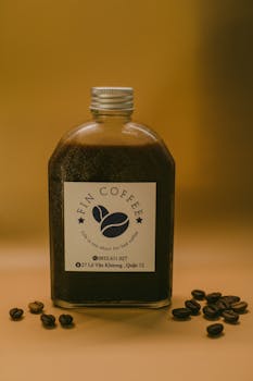 Glass bottle filled with dark coffee and beans on yellow backdrop.