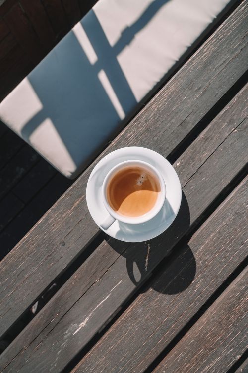 Free A cup of coffee casting a shadow on a wooden table with sunlight and shadow play. Stock Photo