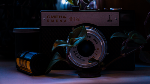 Free A nostalgic still life featuring a vintage Smena 8M camera and film roll, surrounded by leaves. Stock Photo