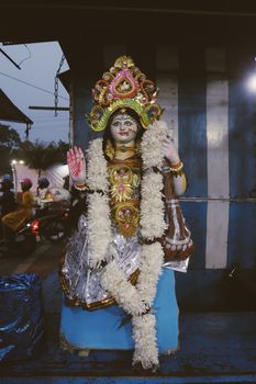 A vibrant Hindu goddess statue adorned with a floral garland in an outdoor setting.