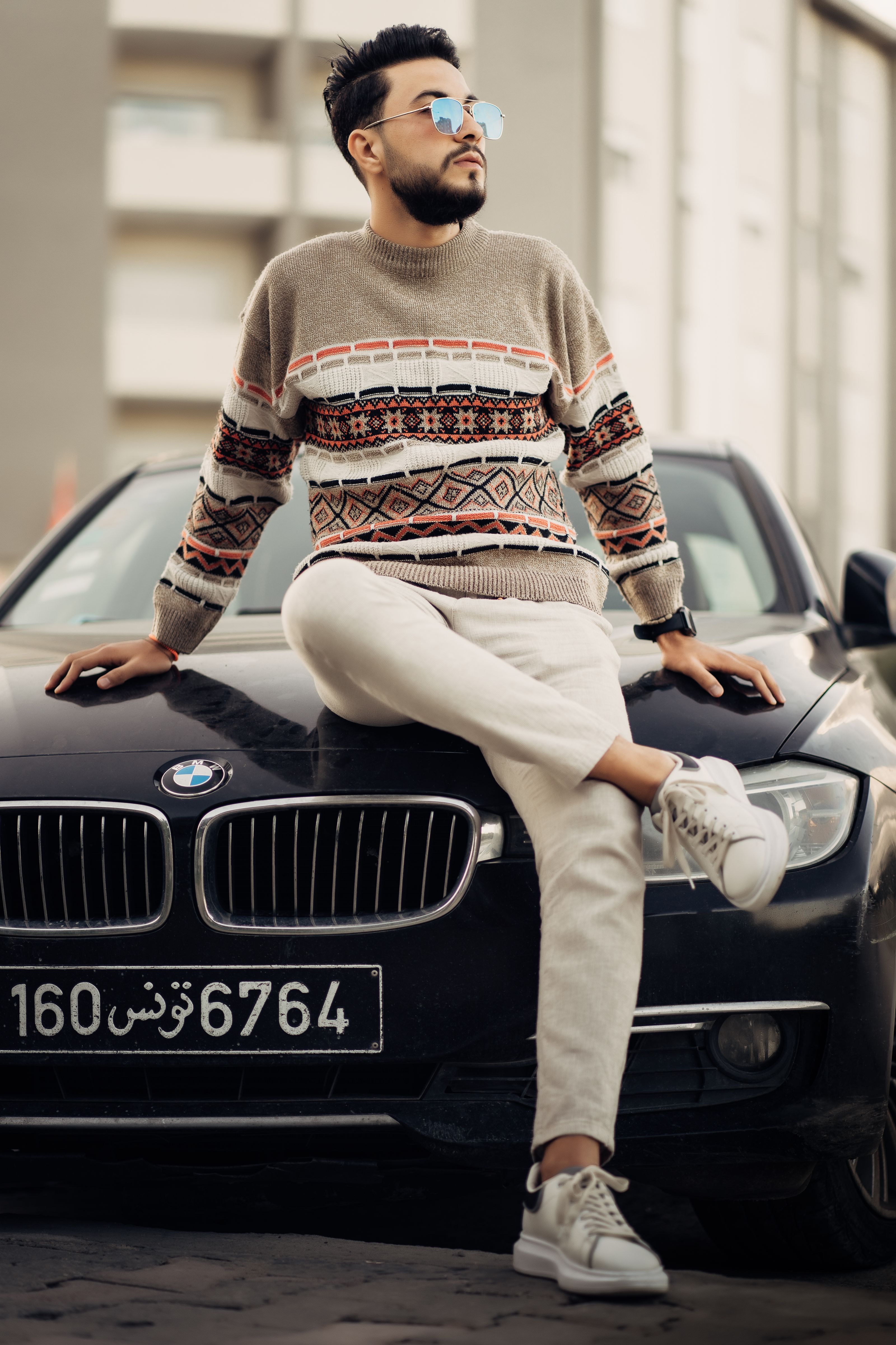 Um homem fashion de óculos de sol posa em um BMW em Hammamet, exibindo elegância casual.