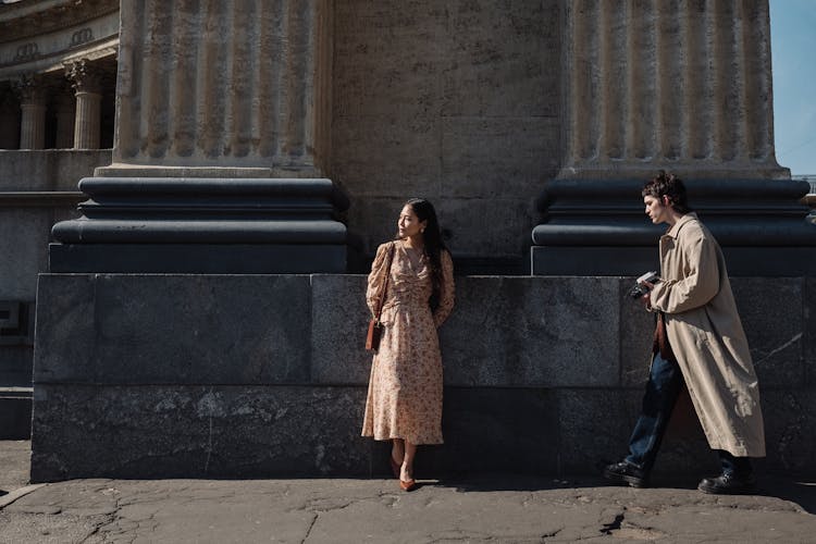 Woman Standing In Front Of Colonnade and Man With Camera Coming To Her