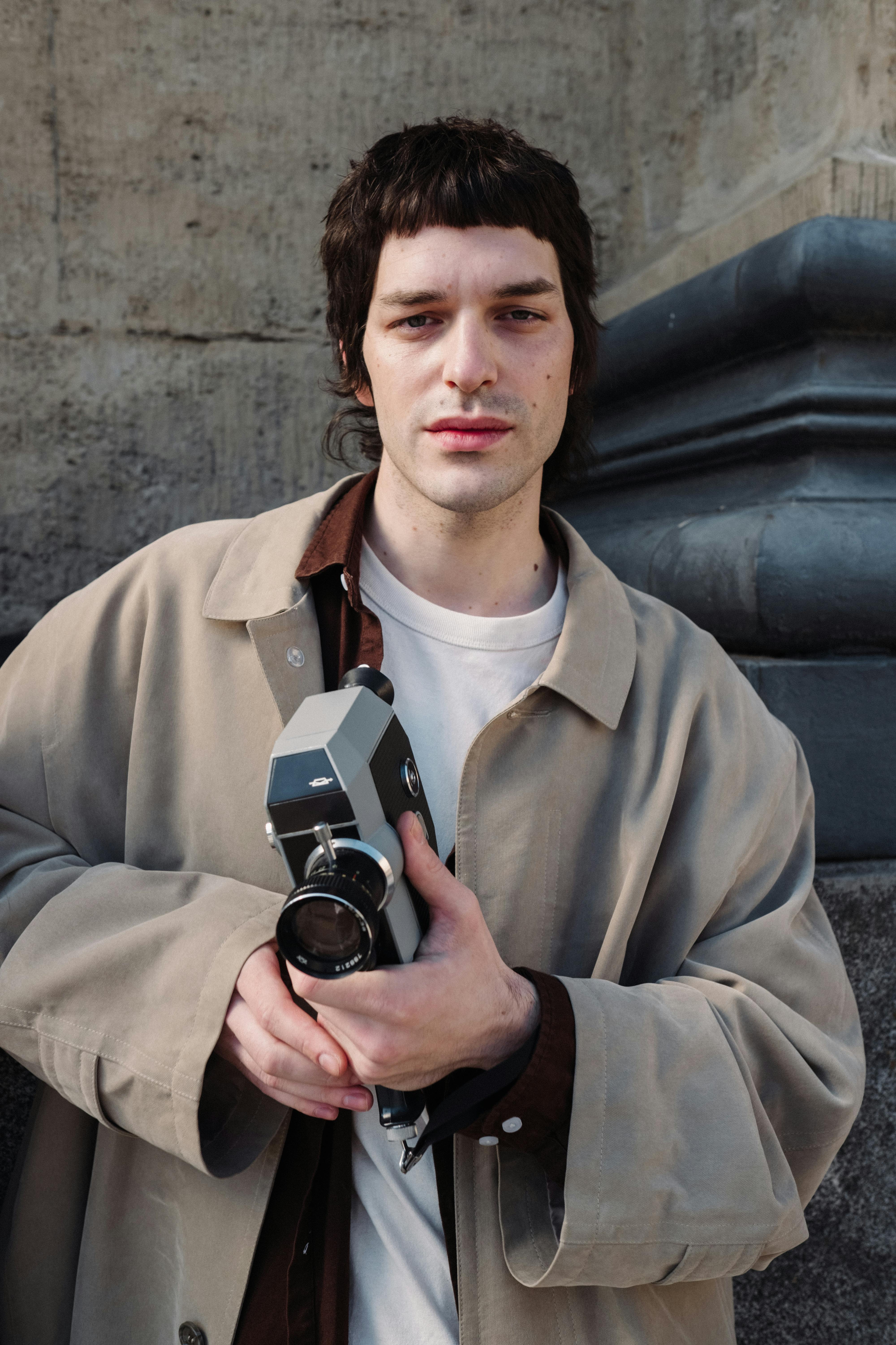 Portrait of a man holding a vintage camera outdoors against stone architecture.