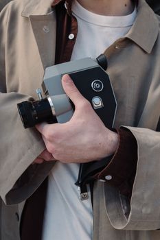 Close-up of a person in a beige coat holding a vintage analog camera.