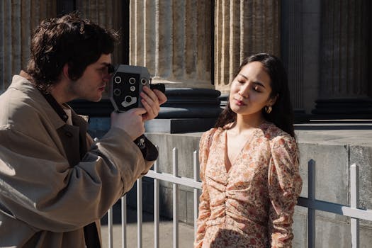 A young couple using an analog camera outdoors by architectural columns.