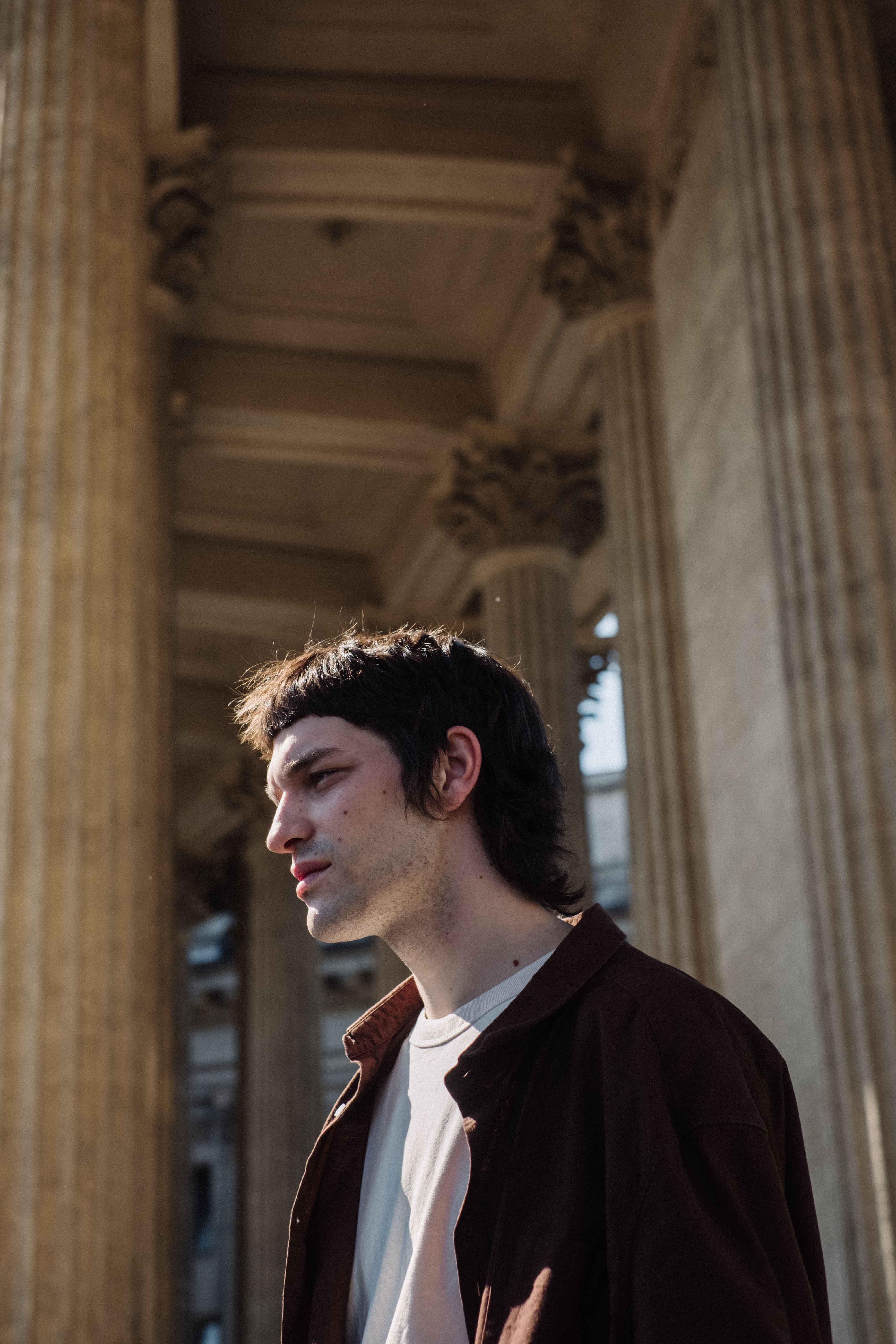 Profile of a man standing among tall classical columns, showcasing architectural elegance.