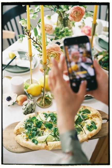 A bright, styled brunch table with floral decor and gourmet pizza captured on a smartphone.