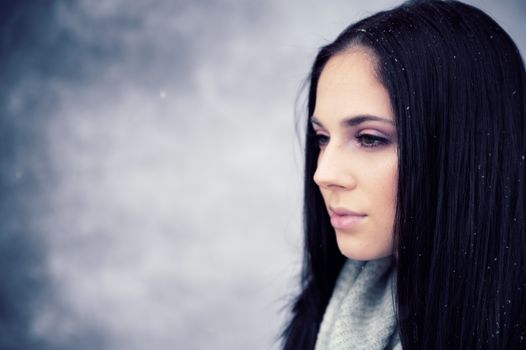 Portrait of a woman with long black hair in a winter setting, snowflakes on her hair.