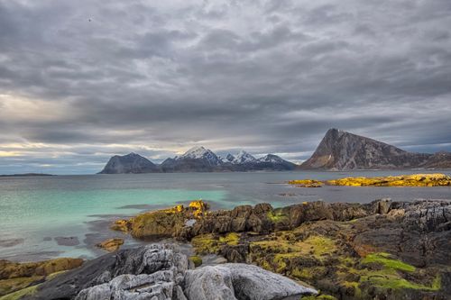 Free Dramatic rocky coastline with mountains in Storsandnes, Norway, under a cloudy sky. Stock Photo