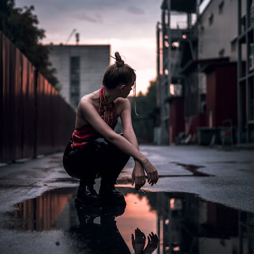 Woman Crouching in a Puddle on a Street 