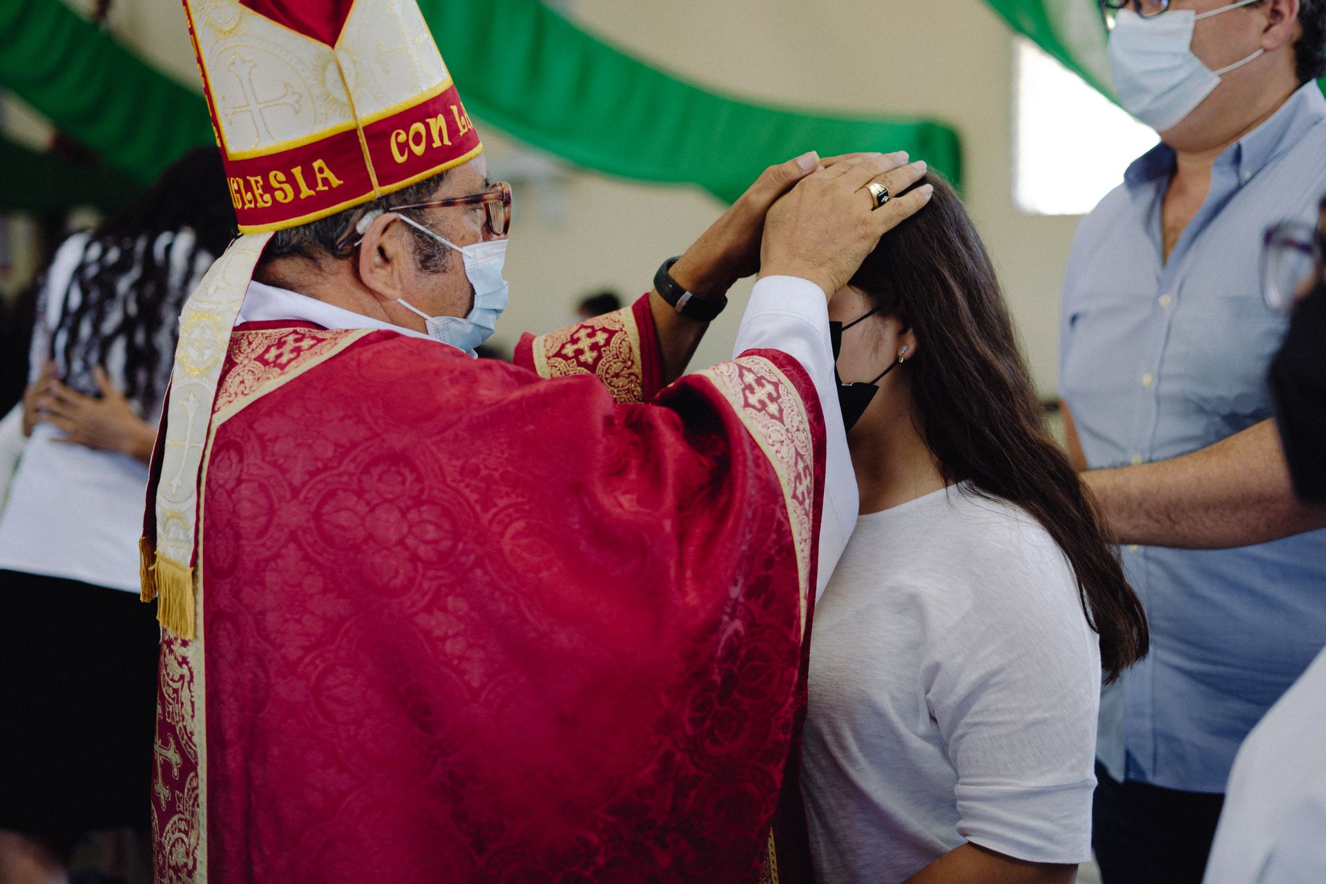 A bishop performs a confirmation on a teenager in a traditional religious ceremony.