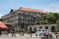 A classic college building surrounded by vibrant urban life and trees.