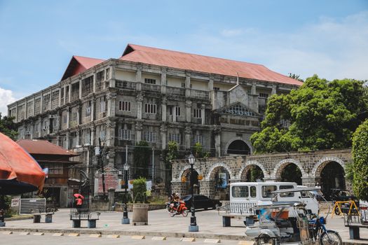 A classic college building surrounded by vibrant urban life and trees.