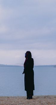 Silhouette of a woman in a black coat by a tranquil lake in Baymak, Russia.
