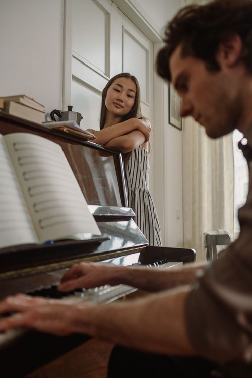 Free Woman watches man play piano, creating a serene and intimate musical moment indoors. Stock Photo