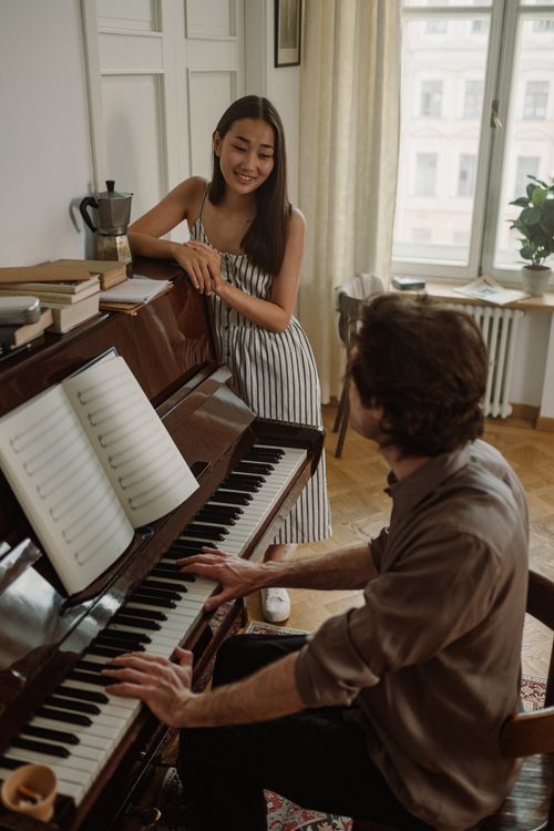 Free A young woman enjoys listening to a man playing the piano in a cozy indoor setting. Stock Photo
