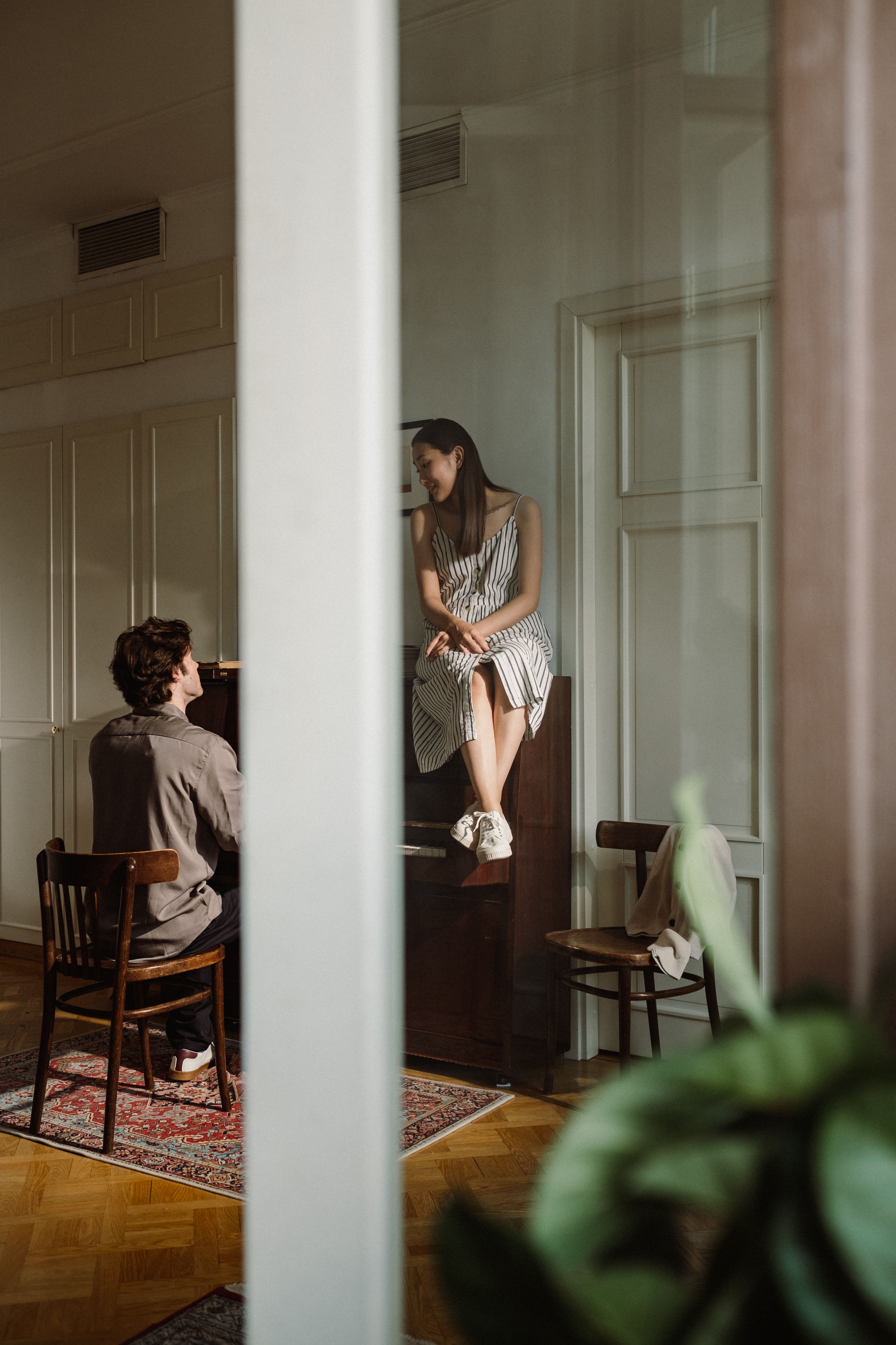 A man playing piano while his partner listens closely beside him, a quiet moment of shared attention