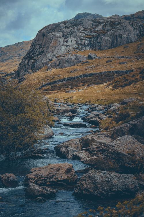 Free Tranquil creek flowing between rocks with mountain backdrop, showcasing natural beauty and rugged landscapes. Stock Photo