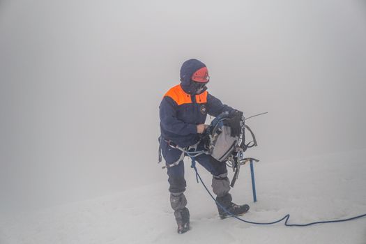 A climber adjusting gear in snowy, foggy conditions, showcasing adventure and winter preparedness.