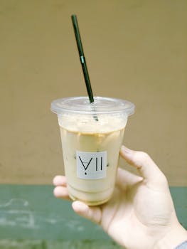 Refreshing iced coffee in a plastic cup with a straw held in hand.