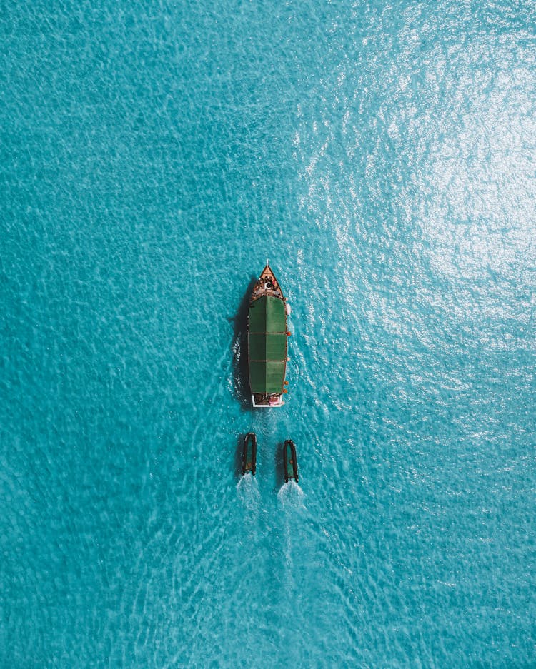 Boat Sailing Through Ocean Water With Wake Boards Behind