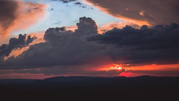 Um pôr do sol deslumbrante com nuvens dramáticas sobre montanhas no Brasil, capturando a beleza da natureza.