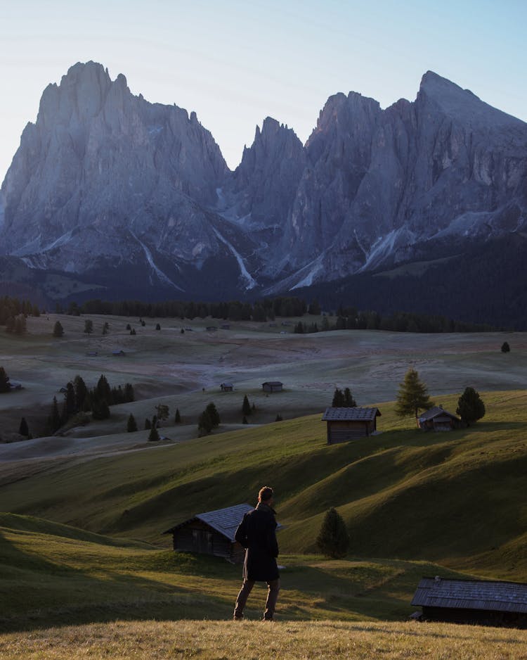 A Shot From Behind Of A Male Standing On Hill And Looking At Mountains