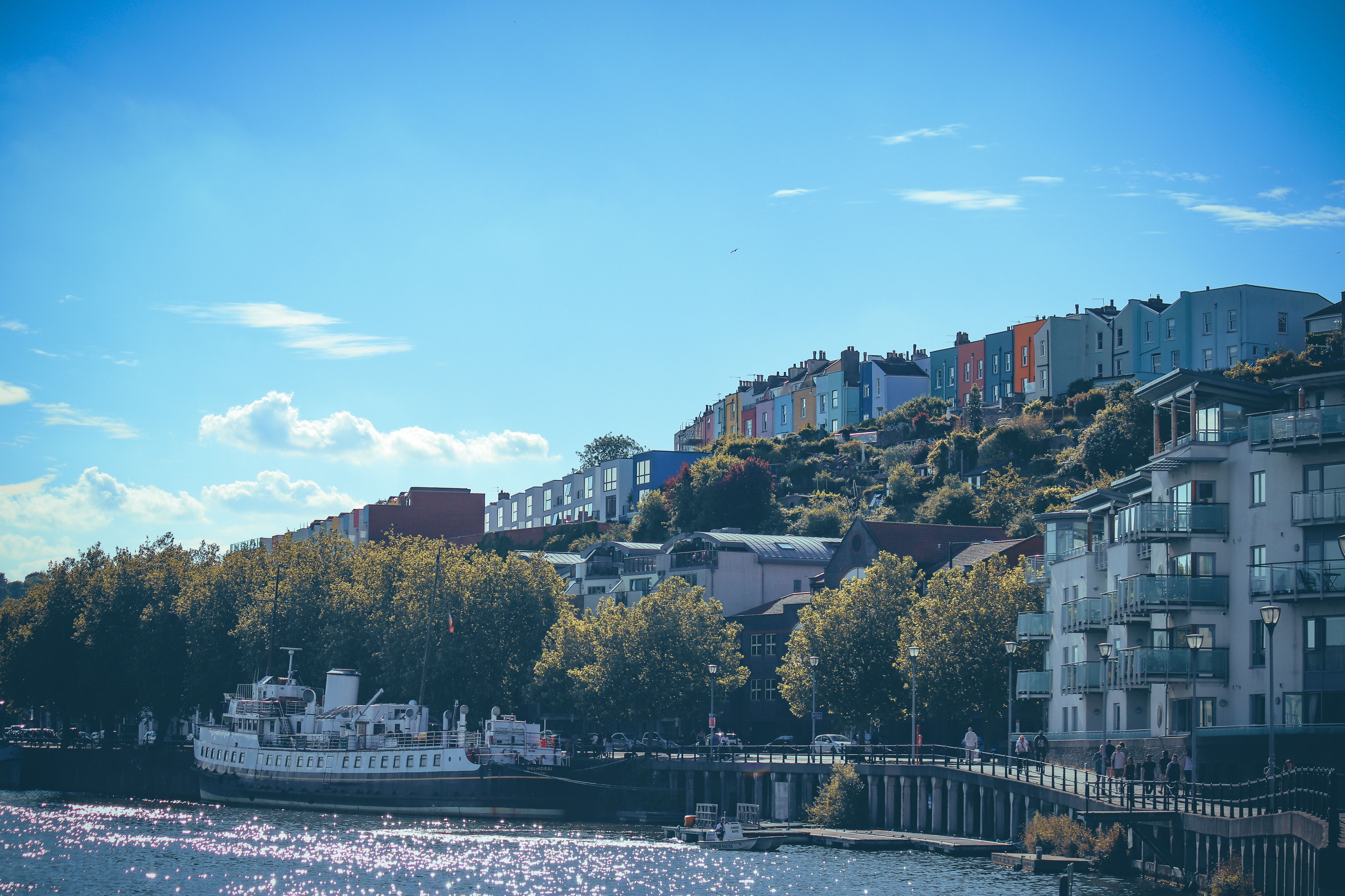 Beautiful view of Bristol's harbourside with colourful houses and a riverboat under a clear blue sky.