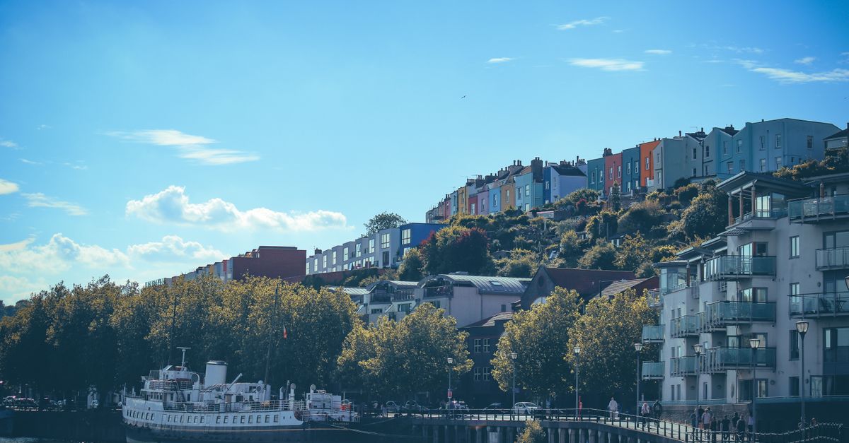 Beautiful view of Bristol's harbourside with colourful houses and a riverboat under a clear blue sky.
