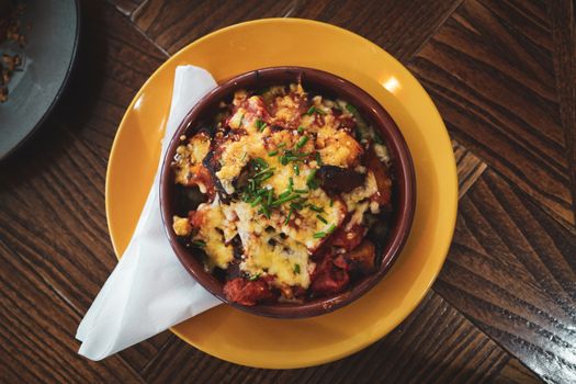 A flavorful baked cheese and vegetable dish served in a bowl on a wooden table.