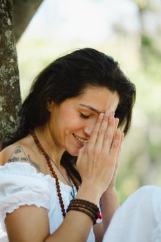 A peaceful woman with hands clasped in prayer, meditating outdoors on a sunny day.