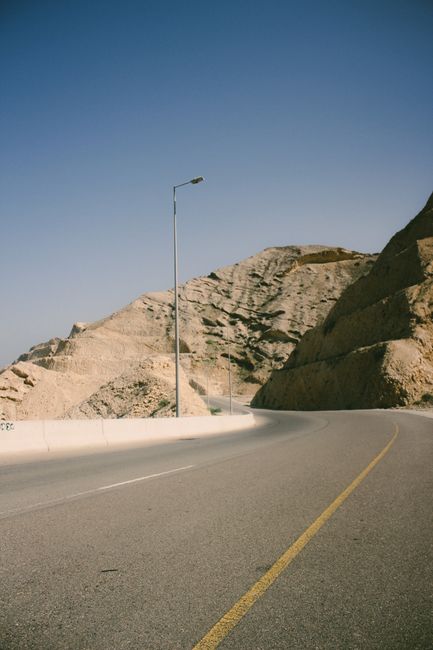 Empty desert road in Muscat, Oman with rugged mountains under a clear blue sky.